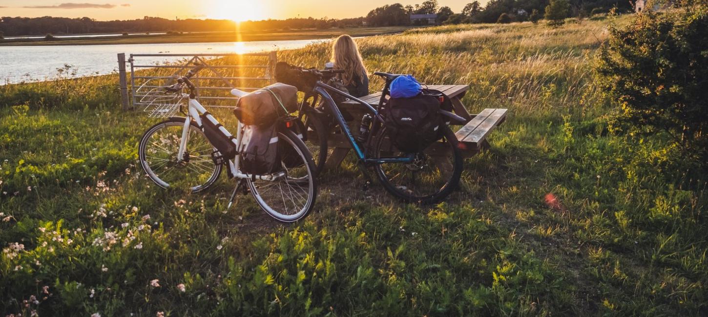 Kvinne slapper av ved et bord og en benk, midt på et jorde, og beundrer soloppgangen over vannet ved knudshoved på Fyn