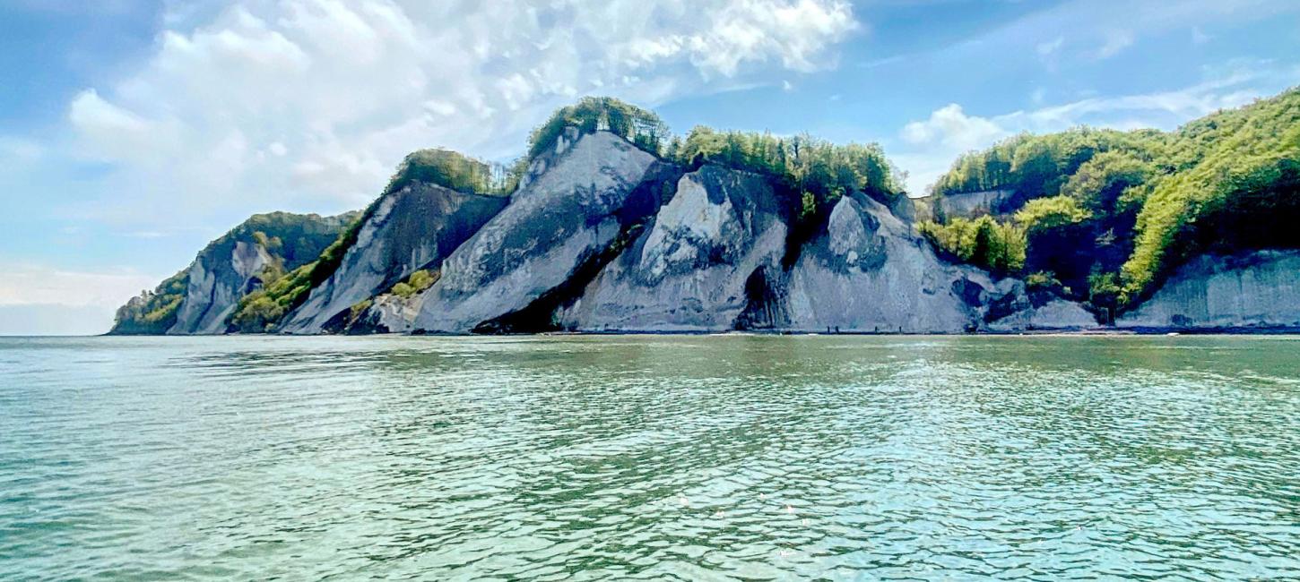 Das Bild zeigt einen blauen Himmel, türkisfarbenes Meer und die Klippen von Møn. 